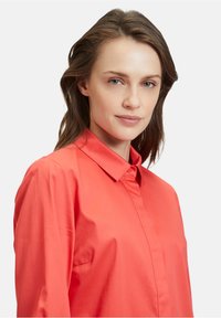 Korallenfarbiges Hemd mit Button-Down-Kragen, aus glattem Stoff gefertigt, mit einer Knopfleiste vorne und taillierter Passform.