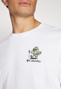 Bijela pamučna majica s motivom zelenog crtanog vidre sa sunčanim naočalama, koja drži planinarske štapove, a ispod je crni natpis "Columbia".