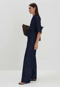 Dark denim matching set featuring a short-sleeve shirt with pockets and wide-leg pants, accented by contrasting stitching. Woven bag included.