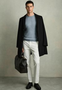 Fekete kabát világoskék pulóver felett, fehér nadrág, fekete bőr táska és fekete csizma. Sima textúra, testre szabott dizájn és minimalista kiegészítők.