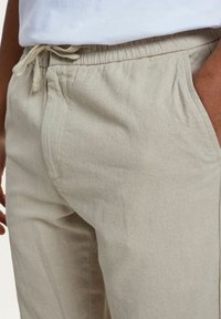 Beige linnen broek met een elastische tailleband en trekkoord. Voorzien van zijzakken en een ontspannen pasvorm. Vlakke textuur met minimale stikseldetails.