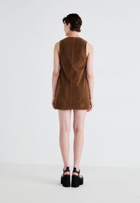 Brown suede sleeveless dress with a straight silhouette, featuring a central back seam. The model wears black platform sandals.