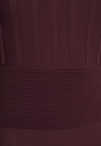 Tissu en tricot de couleur marron foncé avec nervures verticales et rayures horizontales, doté d'une bande inférieure lisse. Matière douce et extensible.