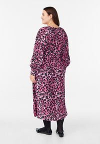 Roza in črna leopardja obleka z dolgimi rokavi, z zategnjeno pasom in ohlapno silhueto. Oblečena s črnimi balerinkami in najlonkami.