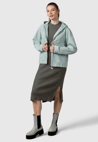 Giacca azzurro chiaro con cappuccio, vestito grigio a coste con uno spacco laterale e stivaletti grigi alla caviglia con suola nera spessa e lati elastici.