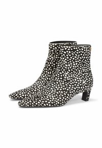 Botas negras de tobillo con lunares irregulares blancos, punteras afiladas y tacones bajos, mostradas una al lado de la otra sobre un fondo blanco.