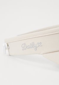 Beige canvas bucket hat with a rounded brim and embroidered "Daily" in silver. Features a drawstring for adjustable fit.