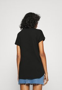 Musta lyhythihainen t-paita, jossa on rento istuvuus, pyöristetty helma ja pehmeä puuvillamateriaali; yhdistetty kuluneeseen farkkuhameeseen.