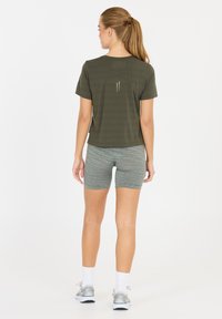 Olivgrön atletisk t-shirt med korta ärmar, detaljer på bakpanelen och reflexband, tillsammans med grå randiga shorts.