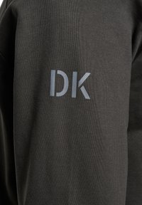 Ciemnoszary materiał swetra o fakturowanym wykończeniu, z jasnoszarym logo "DK" na rękawie.