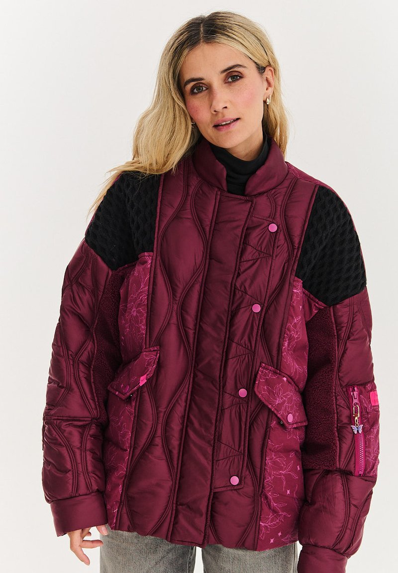 Bordový oversize puffový kabát s textúrovanými čiernymi rukávmi, horizontálnym prešívaním, ružovými gombíkmi a akcentovým zipsovým vreckom.