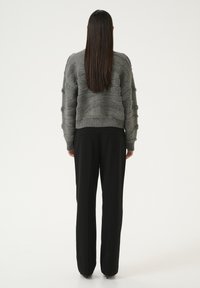 Maglione grigio a trama con un design ondulato e orlo a coste, abbinato a pantaloni neri a gamba dritta e scarpe con tacco.