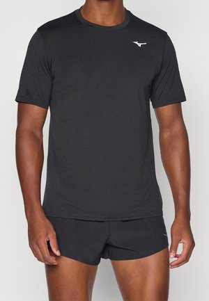 Hombre con una camiseta deportiva negra de manga corta y pantalones cortos negros para correr, de pie sobre un fondo sencillo.