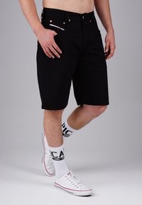 Black denim shorts with a straight cut, featuring a waistband with belt loops, and copper-tone hardware. Worn with white socks and sneakers.