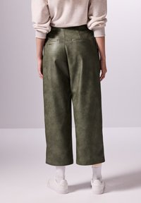 Gröna konstlädervidbyxor med hög midja och bakfickor, kombinerade med vita sneakers och ankellånga strumpor.