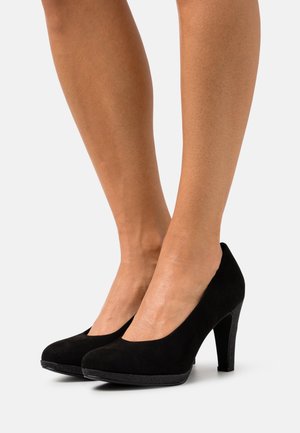 Escarpins en suede noir avec un bout arrondi, texture lisse et un talon stiletto de hauteur intermédiaire. Le design présente un léger éclat sur la semelle.