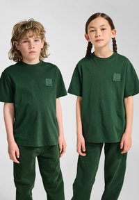 Grønne bomulds t-shirts med korte ærmer og lomme, parret med matchende grønne bukser. Enkle, afslappede pasform og glat tekstur.