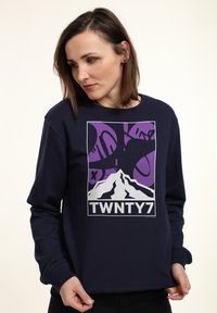 Felpa blu navy con grafica di montagna bianca e accenti viola, con il testo "TWNTY7" in basso, realizzata in morbido materiale misto cotone.