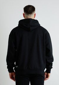 Czarna bluza z kapturem o luźnym kroju, wykonana z bawełny, z prążkowanymi mankietami i subtelnym logo niedaleko dołu.