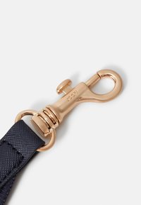 Cintura blu navy con una chiusura a scatto in metallo dorato lucido e dettagli texture. La vista ravvicinata mette in evidenza il materiale e la finitura.