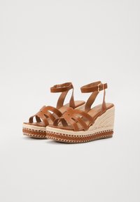 Bruine leren wedge sandalen met kruislings gespen, open teen en enkelbandje. De zool van jute touw heeft een gevlochten accent.