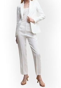 Blazer bianco in lino con pantaloni abbinati, caratterizzato da una vestibilità su misura, una texture sottile e una chiusura con un singolo bottone sulla giacca.