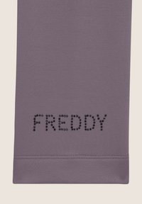 Tela púrpura con la palabra "FREDDY" en strass negros. Textura suave con un borde recto en la parte inferior.