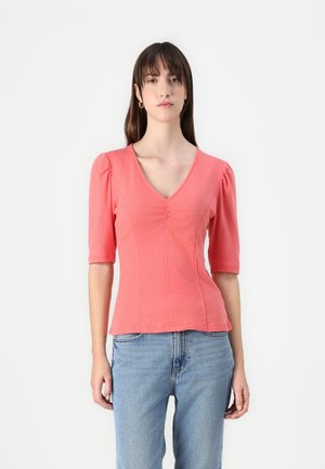 Coral cotton top with a V-neck, short puff sleeves, and a gathered detail at the center. Paired with light blue jeans.
