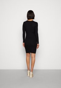 Abito nero a maniche lunghe con lavorazione a coste, dalla silhouette aderente, lunghezza al ginocchio e scollatura rotonda. Indossato con scarpe beige con tacco largo.
