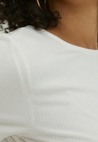 Maglietta bianca a maniche corte con scollatura rotonda. Il tessuto appare morbido e strutturato, mettendo in risalto le righe orizzontali sulla superficie.