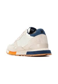 Zapatilla con parte superior de ante beige y sintético blanco, lengüeta trasera azul marino y un acento naranja cerca de la suela; con una suela de goma texturizada.