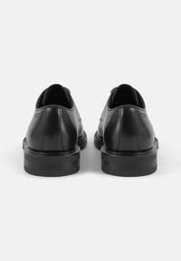 Chaussures en cuir noir avec une finition lisse, un design bas, des bouts arrondis et de épais semelles en caoutchouc. La vue arrière montre un branding minimaliste.