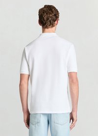 Polo blanc à finition texturée, manches courtes, col classique et ourlet droit. Porté avec un jean bleu clair.