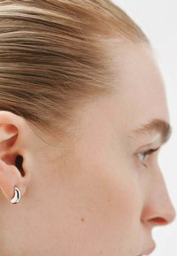 Pendiente de aro en forma de media luna de plata en la oreja de una persona, mostrando un acabado elegante y pulido contra la piel clara y el cabello recogido.