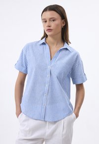Camicia a maniche corte a righe blu e bianche con colletto, chiusura a bottoni e una vestibilità comoda. Il tessuto sembra leggero e ha una consistenza liscia.