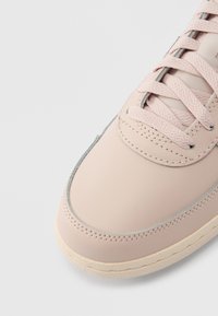 Ανοιχτό ροζ δερμάτινο αθλητικό παπούτσι με στρογγυλεμένη μύτη, επίπεδα κορδόνια και υφασμένη μπεζ σόλα· διαθέτει ραφές και δια κριτική γκρι λεπτομέρεια.