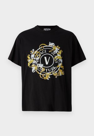 T-shirt noir à manches courtes en coton avec un graphisme circulaire agrémenté de fleurs en blanc et or, affichant le nom de la marque de manière proéminente.