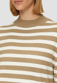 Beiger und weiß gestreifter Pullover mit geripptem Kragen, weich in der Textur und mit mittlerem Strickmuster. Nahaufnahme des Oberkörperbereichs.