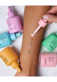 Cinco coloridos frascos de suero rodean una aplicación de cinco gotas sobre un brazo de tono de piel: rosa, naranja, verde, lavanda y azul verdoso. Los frascos tienen goteros.