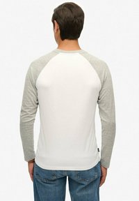 Koszula z długim rękawem o białym korpusie i jasnoszarych rękawach raglanowych. Teksturowana tkanina z zaokrąglonym dołem, w połączeniu z niebieskimi dżinsami. Prosty design.