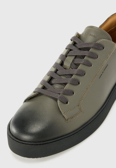 Baskets en cuir vert avec un bout de chaussure foncé, lacets gris, forme arrondie et détails de couture subtils le long du côté. Texture lisse.
