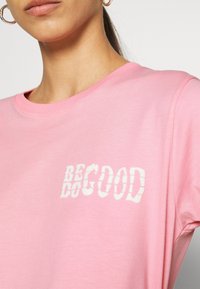 Růžové bavlněné tričko s kulatým výstřihem a krátkými rukávy, s bílým potiskem "BE GOOD" na přední straně.