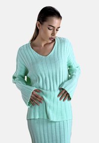 Minzgrüner gerippter Pullover mit V-Ausschnitt, langen Glockenärmeln und lockerer Passform. Die Textur ist weich mit einem dezenten Glanz.