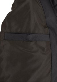 Svart stoff med en horisontal svart meshstripe sydd over midten på en teksturert tekstilbakgrunn.