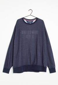 Námořnický modrý sweatshirt Tommy Hilfiger s elastickými manžetami a lemem, s vyraženým nápisem "HILFIGER N.Y.C", zavěšený na černém ramínku.