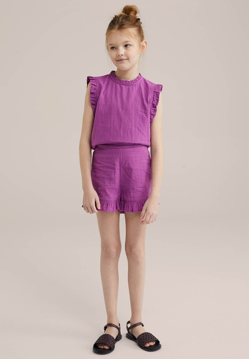 Completo composto da top viola arricciato e pantaloni corti abbinati realizzato in tessuto leggero. I pantaloni corti presentano un orlo fronzoso e il modello indossa sandali neri.