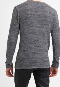 Suéter de punto texturizado gris con mangas largas, cuello redondo y detalles de aberturas laterales. La tela presenta un patrón tejido para mayor profundidad.