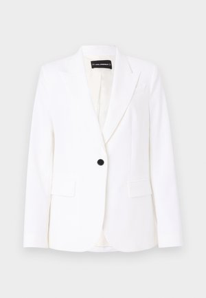 Blazer alb, ajustat, realizat dintr-un material neted, având un singur nasture negru, rever subtire și două buzunare frontale. Interiorul este căptușit.