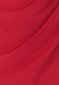 Červená textília s hladkou, jemnou textúrou, so závesmi vytvárajúcimi vlnovitý vzhľad na povrchu.