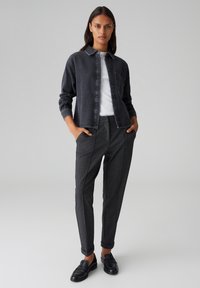 Giacca di jeans scura, t-shirt bianca e pantaloni grigi su misura con una finitura testurizzata. Mocassini neri completano l'outfit.